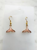 Whale tail shaped earrings on a marble background. 