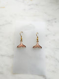 Whale tail shaped earrings on a marble background. 