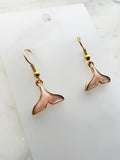 Whale tail shaped earrings on a marble background. 