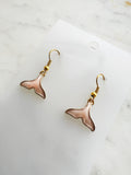 Whale tail shaped earrings on a marble background. 