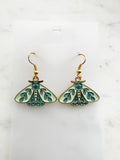 Pair of Kawaii enamel moth dangle earrings featuring pastel mint wings with teal botanical detailing, outlined in gold-tone metal with gold ear hooks, displayed on a marble background.