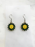 Pair of Kawaii enamel flower dangle earrings featuring green petals with a yellow centre, outlined in silver-tone metal with silver ear hooks, displayed on a marble background.