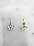 Pair of Kawaii enamel white flower dangle earrings featuring five-petal white blossoms with gold centers and gold-tone outlines, displayed on a marble background.