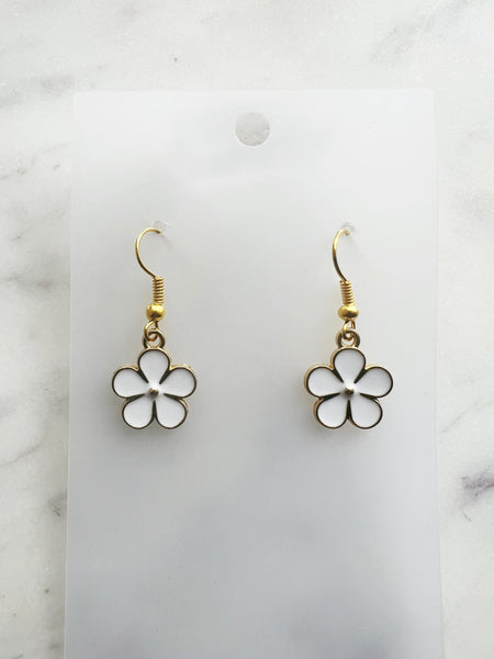 Pair of Kawaii enamel white flower dangle earrings featuring five-petal white blossoms with gold centers and gold-tone outlines, displayed on a marble background.