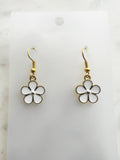 Pair of Kawaii enamel white flower dangle earrings featuring five-petal white blossoms with gold centers and gold-tone outlines, displayed on a marble background.