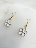 Pair of Kawaii enamel white flower dangle earrings featuring five-petal white blossoms with gold centers and gold-tone outlines, displayed on a marble background.