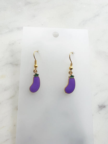 Pair of Kawaii enamel eggplant dangle earrings featuring purple eggplants with green tops, outlined in gold-tone metal with gold ear hooks, displayed on a marble background.