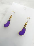 Side view of a Pair of Kawaii enamel eggplant dangle earrings featuring purple eggplants with green tops, outlined in gold-tone metal with gold ear hooks, displayed on a marble background.