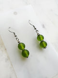 Side view of a Pair of handmade frosted green vintage glass bead earrings with two stacked 10mm beads on nickel-free ear hooks, displayed on a marble backing card.