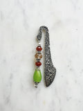 Handmade antique silver bookmark with ornate etched pattern, featuring Tibetan silver bead caps and beads in amber, red, and a lime-green teardrop, displayed on a marble background.