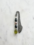 Handmade antique silver bookmark with ornate etched pattern, featuring black faceted beads, a mauve pearl bead, and an olive-green faceted teardrop with Tibetan silver bead caps, displayed on a marble background.