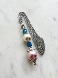 Handmade antique silver bookmark with ornate etched design, featuring blue cube beads, a faceted bead, and a pearl accent, displayed on a marble background.