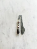 Handmade antique silver bookmark with ornate etched pattern, featuring mauve glass pearl beads, a champagne crystal bead, and a glass plum teardrop bead with Tibetan silver bead caps, displayed on a marble background.