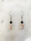 Handmade blush pink faceted crystal dangle earrings with black glass accent beads, Tibetan silver spacers, and surgical stainless steel hooks, displayed on a marble background.