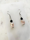 Handmade blush pink faceted crystal dangle earrings with black glass accent beads, Tibetan silver spacers, and surgical stainless steel hooks, displayed on a marble background.