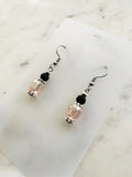 Handmade blush pink faceted crystal dangle earrings with black glass accent beads, Tibetan silver spacers, and surgical stainless steel hooks, displayed on a marble background.