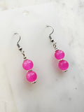 Handmade candy pink vintage glass bead dangle earrings with two fluorescent translucent beads on surgical stainless steel hooks, displayed on a white card background with Tibetan silver spacers