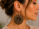 A close-up side profile of a woman wearing a large, ornate black filigree dangle earring.