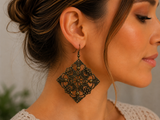 A close-up side profile of a woman wearing a large, ornate filigree dangle earring with a warm bronze-toned finish.