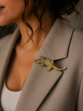 A close-up of a woman wearing a textured gold crocodile brooch pinned to her taupe blazer.