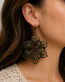 A close-up of a woman wearing a large, ornate filigree dangle earring in an antique bronze finish.