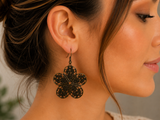 A close-up side profile of a woman wearing a large black filigree flower-shaped dangle earring.