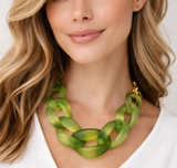 Woman wearing a Chunky frosted acrylic chain necklace in translucent green tones, with large twisted links and a polished gold-tone clasp, displayed on a plain background