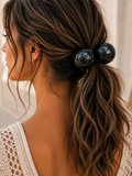 A close-up side view of a woman with long, wavy brown hair wearing a black marbled two-blob hair tie in her low ponytail.