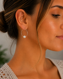 A close-up of a woman wearing a delicate silver hoop earring with a single white pearl drop, shown from the side profile.