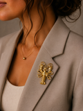 A close-up of a woman wearing a gold lobster-shaped brooch pinned to her beige blazer.