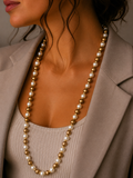 A close-up of a woman wearing a long double-strand necklace made of alternating white pearls and polished gold beads, styled with a beige blazer and ribbed top.