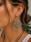 A close-up of a woman wearing a large circular silver filigree dangle earring with intricate scrollwork.