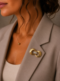 A close-up of a woman wearing a gold-toned double-ring brooch with a clear crystal center, pinned to her taupe blazer.