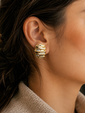 A close-up of a model's ear wearing a gold huggie hoop earring adorned with multiple rows of small clear crystals.