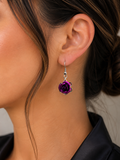A close-up of a model's ear wearing a dangling rose earring. The earring features a deep purple rose charm with a silver-toned metal setting and hook.