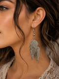 A close-up of a woman wearing a silver dangling earring shaped like a feather or leaf, shown against her ear and neck.
