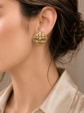 A close-up of a woman wearing a gold geometric stud earring with small clear stones, paired with a champagne satin shirt.