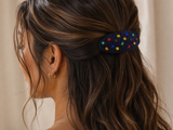 A close-up side view of a woman with long dark brown hair wearing a small oval black beaded hair clip decorated with colorful star-like beads.